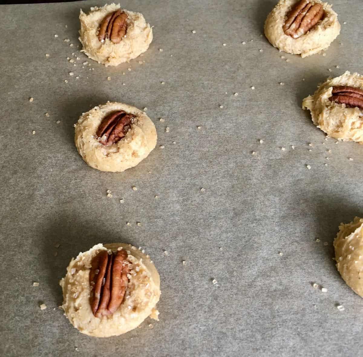 unbaked cookies topped with pecan and sprinkled with sugar